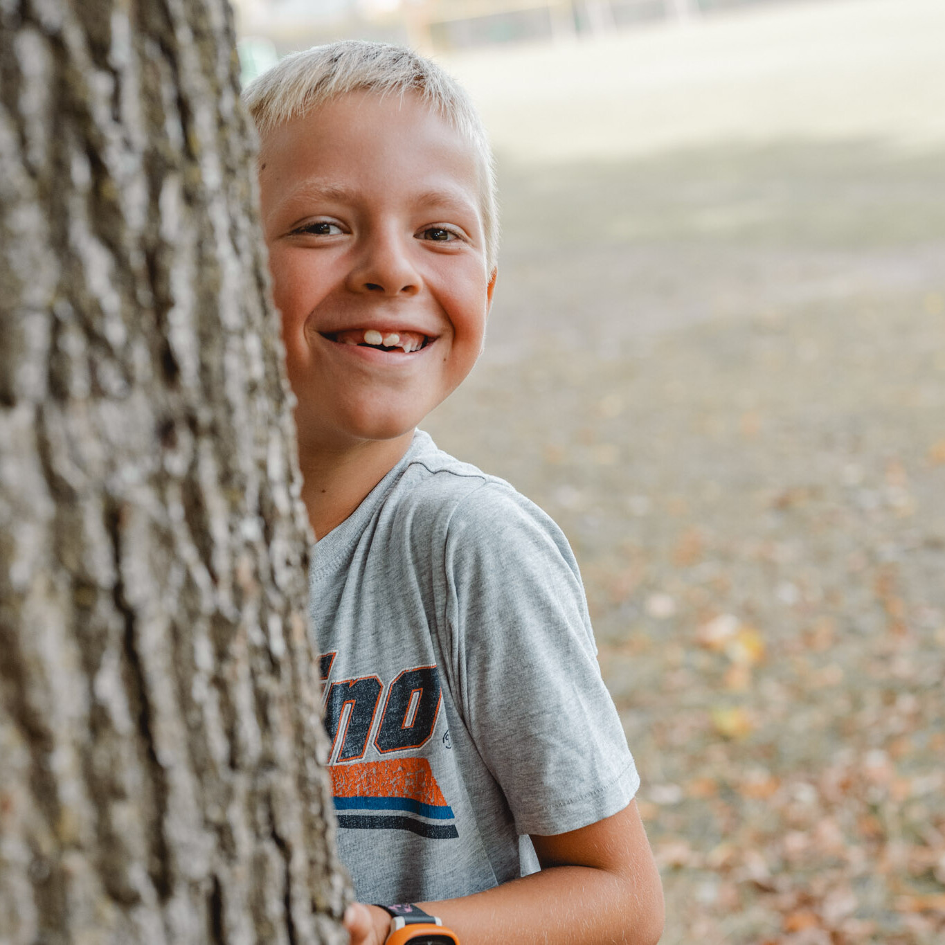 Junge lacht hinter Baum bei der Kitafotografie - natürliche und Lebendige Kitafotogafie